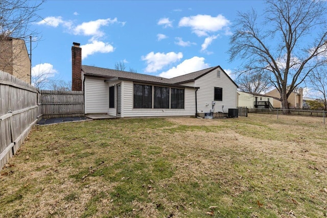 back of property with a fenced backyard, a chimney, central AC unit, and a lawn