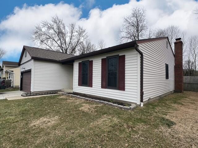 view of side of property featuring an attached garage, fence, driveway, a lawn, and a chimney