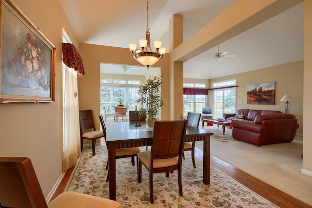 dining room featuring light wood-type flooring, high vaulted ceiling, baseboards, and ceiling fan with notable chandelier