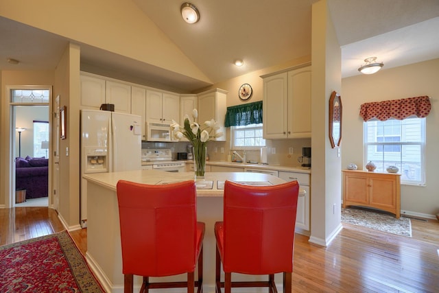 kitchen with light countertops, light wood-style flooring, a kitchen island, vaulted ceiling, and white appliances