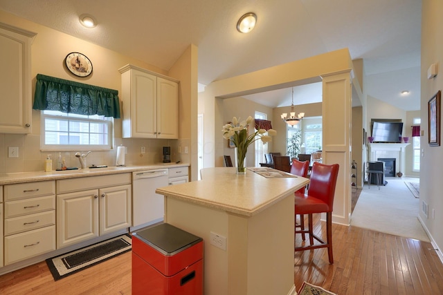 kitchen with decorative backsplash, vaulted ceiling, white dishwasher, a sink, and a chandelier