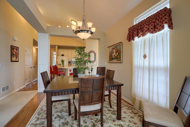 dining room featuring a chandelier, visible vents, baseboards, light wood finished floors, and ornate columns