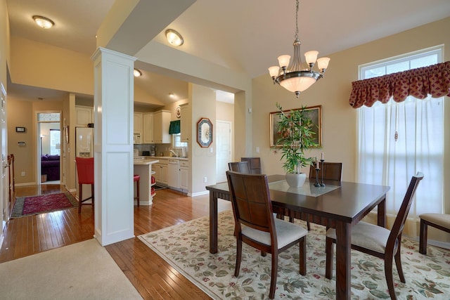 dining area with light wood-style flooring, baseboards, vaulted ceiling, ornate columns, and an inviting chandelier