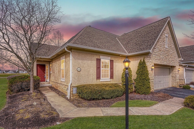 view of front of home featuring aphalt driveway, roof with shingles, stucco siding, an attached garage, and stone siding