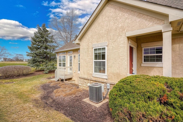 view of side of property featuring a yard, a shingled roof, central air condition unit, and stucco siding