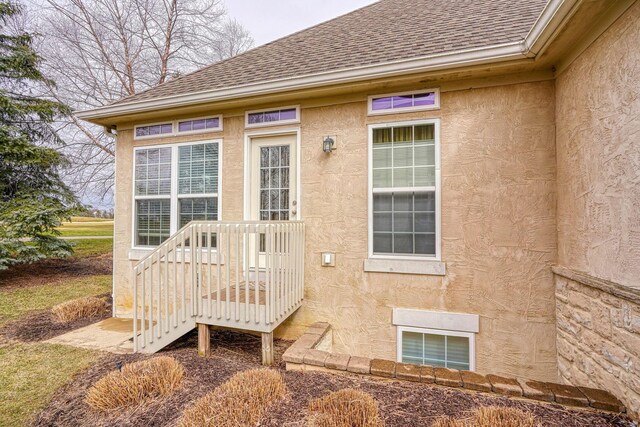 entrance to property featuring stucco siding and roof with shingles