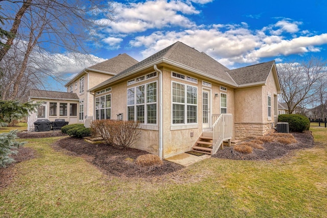 rear view of property featuring cooling unit, stone siding, a lawn, roof with shingles, and stucco siding