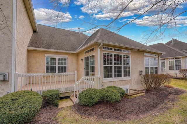 view of side of property featuring a shingled roof, a wooden deck, and stucco siding