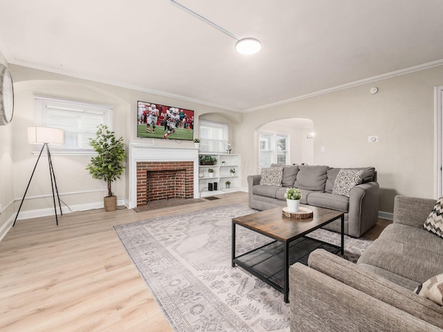 living area featuring arched walkways, a fireplace, baseboards, ornamental molding, and light wood-type flooring