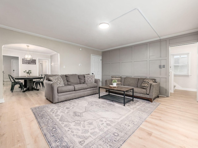 living room featuring ornamental molding, arched walkways, a decorative wall, and light wood finished floors