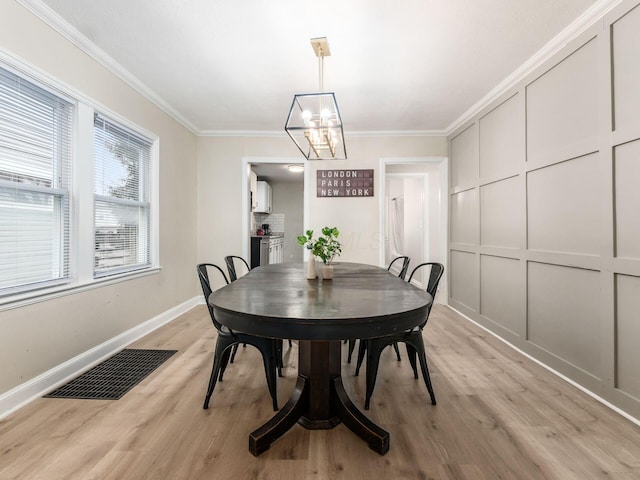 dining area featuring a notable chandelier, a decorative wall, visible vents, ornamental molding, and light wood finished floors