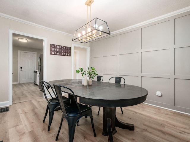 dining area featuring a decorative wall, visible vents, ornamental molding, light wood finished floors, and an inviting chandelier