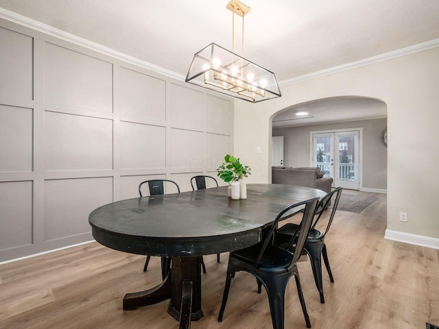 dining room with arched walkways, a decorative wall, ornamental molding, light wood-type flooring, and baseboards