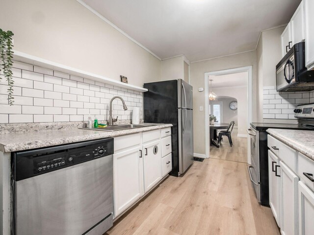 kitchen featuring a sink, white cabinetry, appliances with stainless steel finishes, light wood finished floors, and crown molding