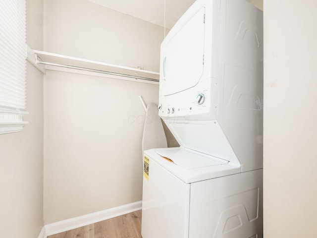 laundry room featuring stacked washer / drying machine, light wood-style flooring, and baseboards