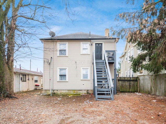 rear view of house featuring a chimney, fence, and stairway