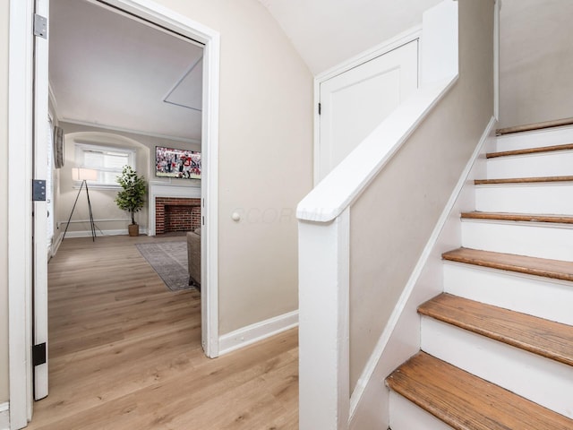 staircase with a fireplace, baseboards, and wood finished floors