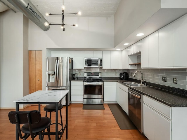 kitchen featuring stainless steel appliances, a sink, light wood-style flooring, and a high ceiling