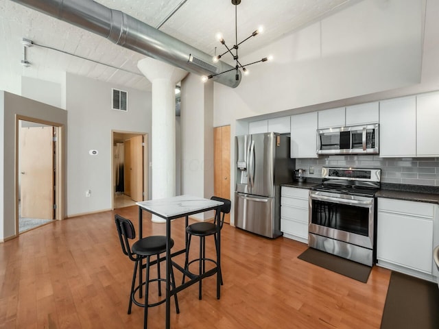 kitchen featuring a towering ceiling, visible vents, appliances with stainless steel finishes, backsplash, and dark countertops