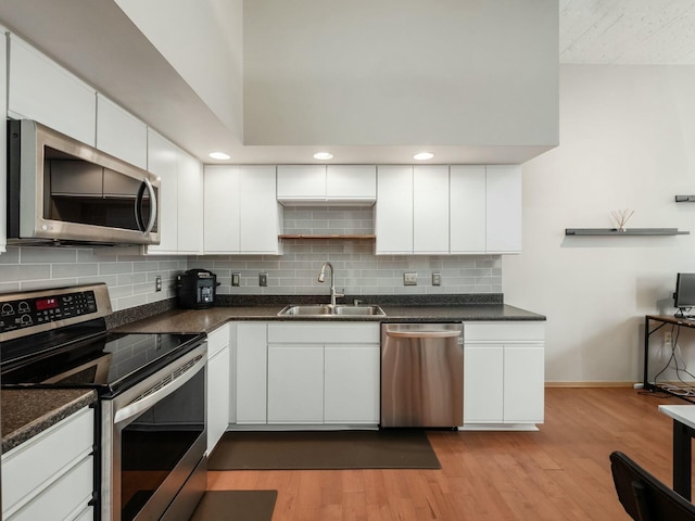 kitchen featuring light wood finished floors, dark countertops, appliances with stainless steel finishes, white cabinetry, and a sink