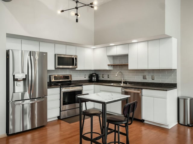 kitchen featuring stainless steel appliances, dark wood-type flooring, a sink, a towering ceiling, and dark countertops