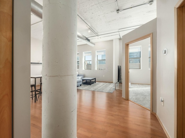 corridor featuring light wood-style floors, rail lighting, and baseboards