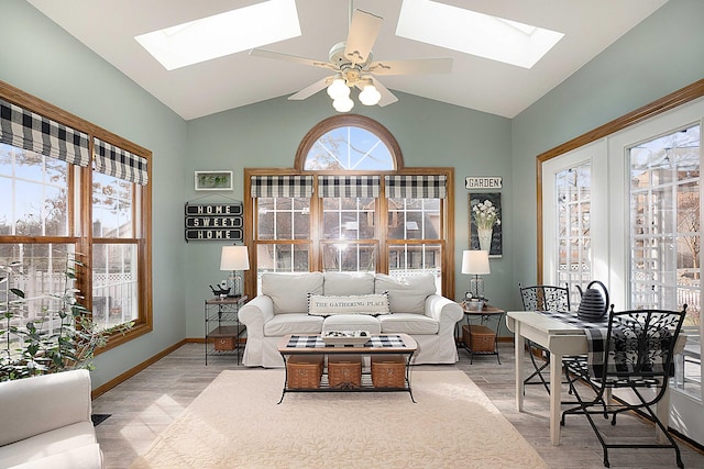 living room with lofted ceiling with skylight, ceiling fan, baseboards, and light wood finished floors