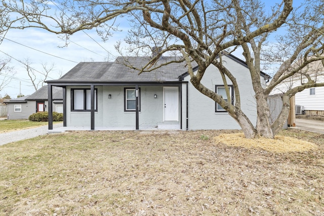 single story home with a porch, brick siding, a front lawn, and roof with shingles