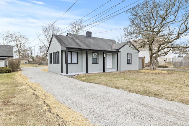 view of front of house with fence, roof with shingles, a front lawn, a chimney, and gravel driveway