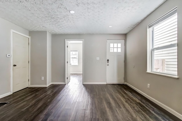 foyer entrance with dark wood-style flooring, a textured ceiling, and baseboards