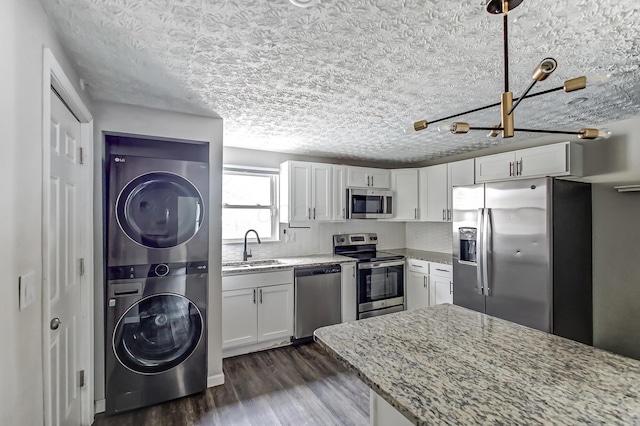 kitchen with light stone counters, stainless steel appliances, stacked washer and dryer, a sink, and dark wood finished floors