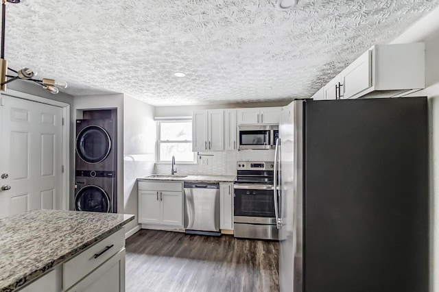 kitchen featuring stacked washer and dryer, dark wood-style flooring, light stone countertops, stainless steel appliances, and a sink