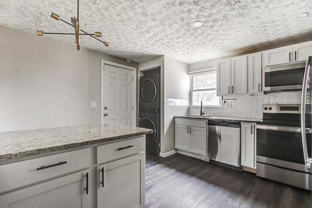 kitchen with light stone countertops, stainless steel appliances, stacked washer / dryer, dark wood-style flooring, and decorative backsplash