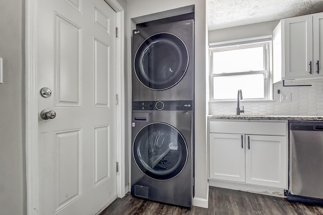 washroom with dark wood-type flooring, stacked washer and clothes dryer, a sink, and laundry area