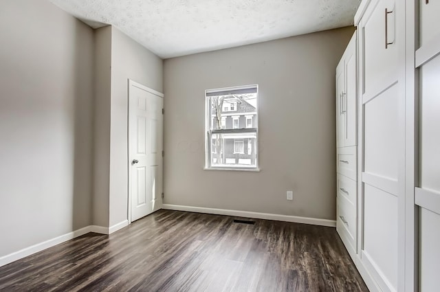 unfurnished bedroom featuring a textured ceiling, baseboards, and dark wood-style flooring