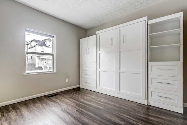 unfurnished bedroom featuring a textured ceiling, dark wood-type flooring, visible vents, baseboards, and a closet