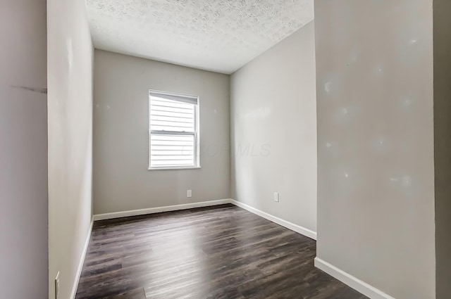 spare room featuring a textured ceiling, dark wood-type flooring, and baseboards