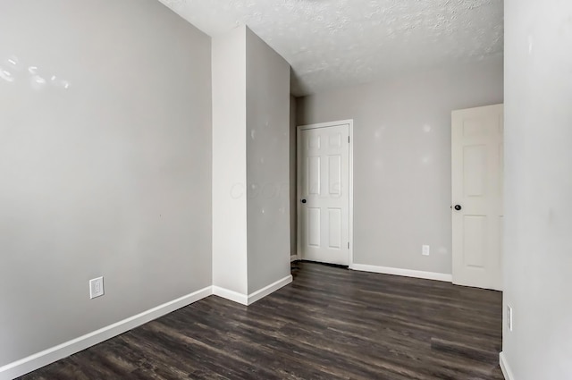 empty room with dark wood-style flooring, a textured ceiling, and baseboards