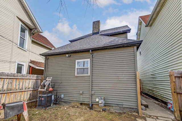 exterior space featuring central AC unit, a shingled roof, a chimney, and fence