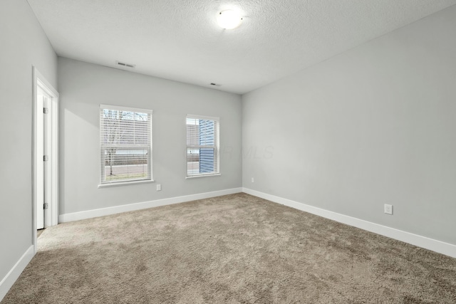 carpeted spare room featuring a textured ceiling, visible vents, and baseboards