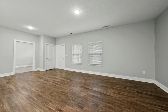 spare room featuring dark wood-style floors, a textured ceiling, visible vents, and baseboards