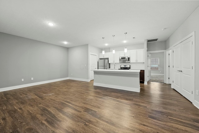 kitchen with visible vents, appliances with stainless steel finishes, dark wood-type flooring, a kitchen island with sink, and baseboards