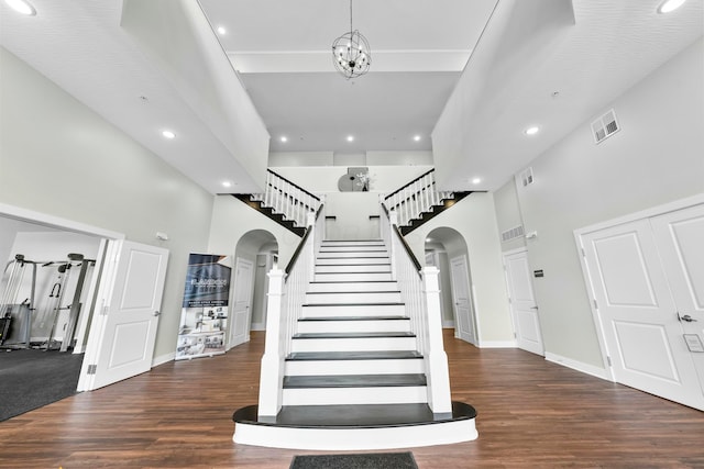 staircase with arched walkways, a high ceiling, wood finished floors, and visible vents