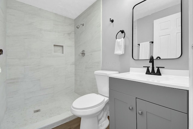 full bathroom featuring tiled shower, toilet, wood finished floors, a textured ceiling, and vanity