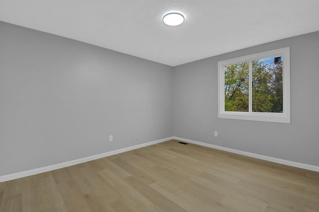 spare room featuring light wood-type flooring, visible vents, and baseboards