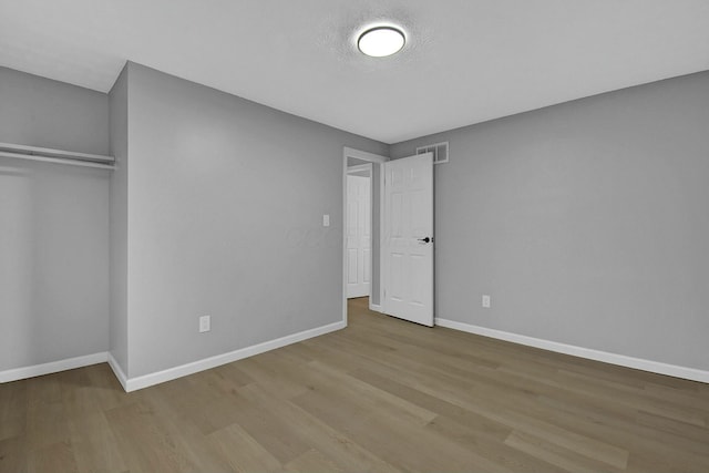 unfurnished bedroom featuring a closet, wood finished floors, visible vents, and baseboards