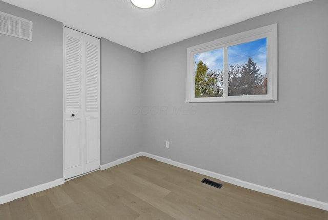 unfurnished bedroom with baseboards, a closet, visible vents, and wood finished floors