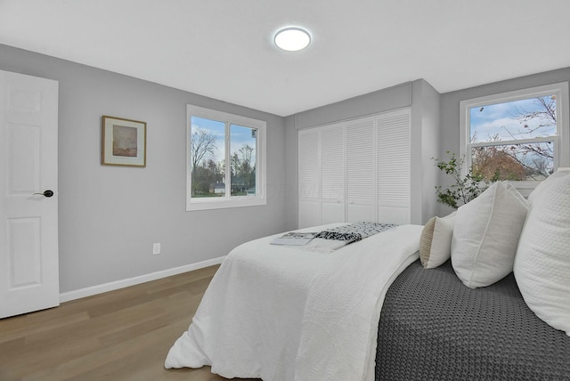 bedroom featuring a closet, multiple windows, baseboards, and wood finished floors