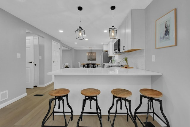 kitchen with stainless steel appliances, tasteful backsplash, light countertops, a peninsula, and a kitchen breakfast bar