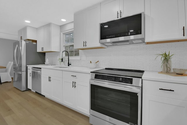 kitchen with light countertops, light wood-style flooring, appliances with stainless steel finishes, white cabinets, and a sink